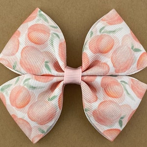 May include: A pink and white bow with a peach print. The bow is made of ribbon and has a pink center.