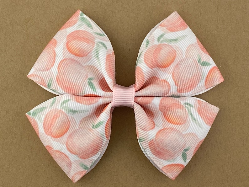 May include: A pink and white bow with a peach print. The bow is made of ribbon and has a pink center.