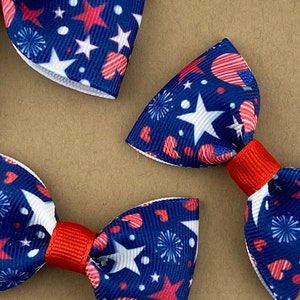 May include: Three red, white, and blue bow ties with a pattern of stars, hearts, and fireworks. The bow ties are made of fabric and have a red center.