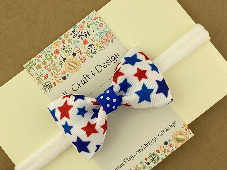May include: A white headband with a red, white, and blue star patterned bow. The bow has a blue polka dot center. The headband is on a white card with the text "Jill Craft & Design" and "www.Etsy.com/shop/jlcraftdesign".
