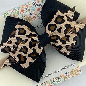 Peut inclure: Un n&oelig;ud noir et beige &agrave; imprim&eacute; l&eacute;opard sur un bandeau beige. Le n&oelig;ud est fait de ruban superpos&eacute; avec une base noire et une couche sup&eacute;rieure &agrave; imprim&eacute; l&eacute;opard. Le bandeau est de couleur neutre.