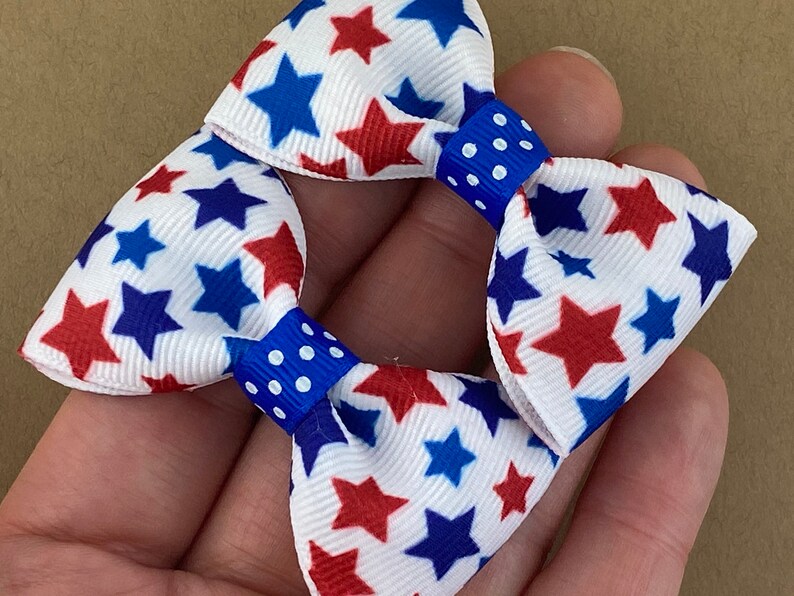 May include: Two red, white, and blue star patterned hair bows with blue and white polka dot centers.