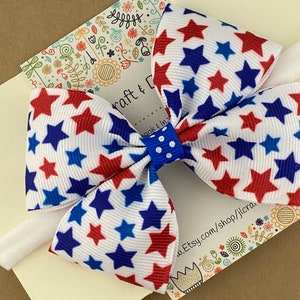 May include: A white headband with a red, white, and blue star patterned bow. The bow is tied with a blue and white polka dot ribbon.