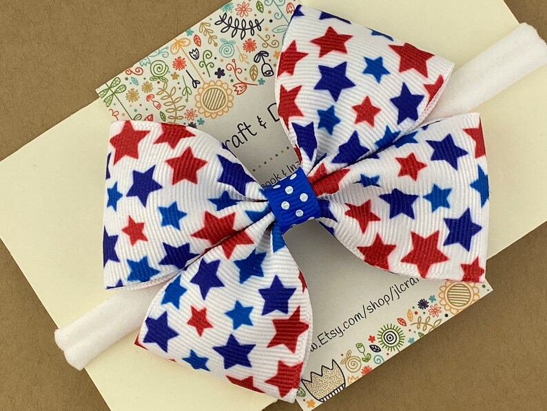 May include: A white headband with a red, white, and blue star patterned bow. The bow is tied with a blue and white polka dot ribbon.