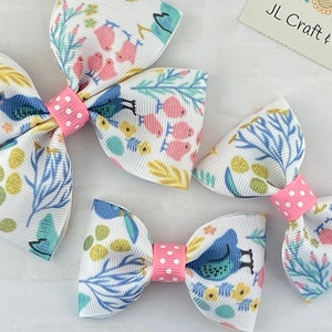 May include: Three white hair bows with a floral and bird print. The bows have pink polka dot centers. The bows are different sizes.