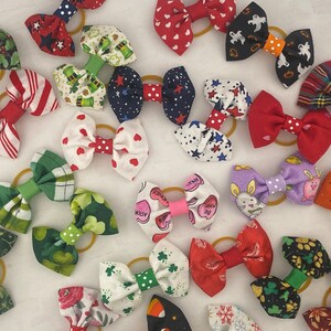 May include: A collection of colorful fabric hair bows with various patterns, including hearts, stars, shamrocks, and animals. The bows are tied with elastic bands and are perfect for adding a touch of whimsy to any outfit.