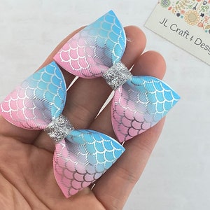 May include: Two pink and blue ombre hair bows with a mermaid scale pattern and silver glitter accents. JL Craft & Design.