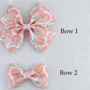 May include: Two peach-patterned hair bows, one large and one small. The larger bow is labeled "Bow 1" and the smaller bow is labeled "Bow 2".