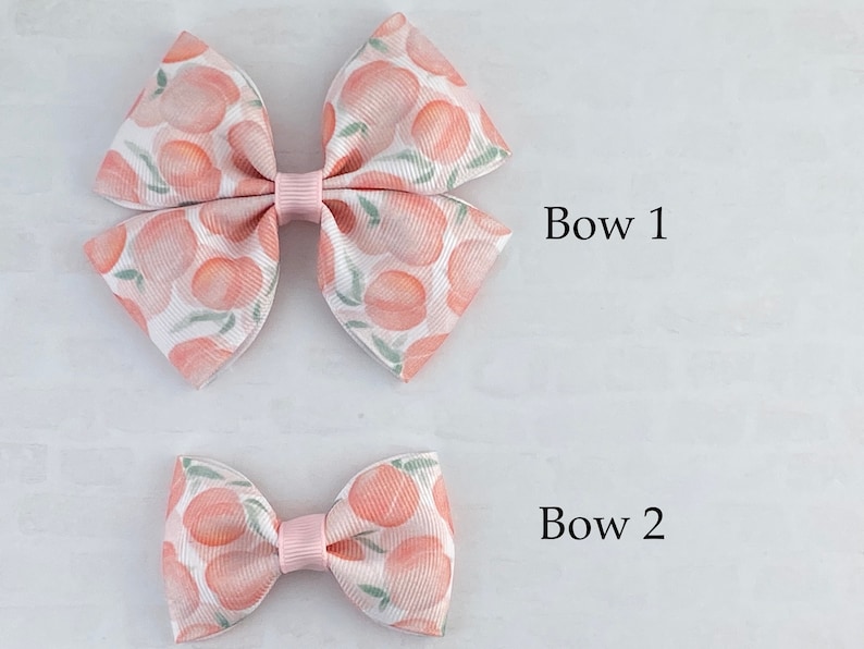 May include: Two peach-patterned hair bows, one large and one small. The larger bow is labeled "Bow 1" and the smaller bow is labeled "Bow 2".