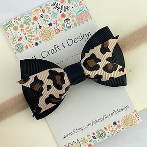 Peut inclure: Un n&oelig;ud noir et beige &agrave; imprim&eacute; l&eacute;opard sur un bandeau beige. Le n&oelig;ud est centr&eacute; sur une carte cr&egrave;me avec le texte "J Craft & Design" et une adresse de site Web. Le fond est beige clair.