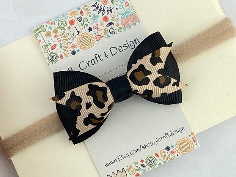 Peut inclure: Un n&oelig;ud noir et beige &agrave; imprim&eacute; l&eacute;opard sur un bandeau beige. Le n&oelig;ud est centr&eacute; sur une carte cr&egrave;me avec le texte "J Craft & Design" et une adresse de site Web. Le fond est beige clair.
