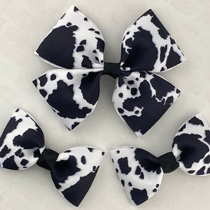 May include: Three black and white cow print hair bows. The largest bow is about 4 inches wide, the smaller bows are about 2 inches wide.