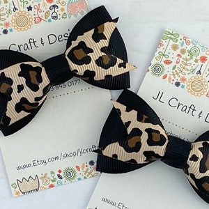 Peut inclure: Deux n&oelig;uds pour cheveux noirs et imprim&eacute; l&eacute;opard beige et marron. Les n&oelig;uds sont sur une carte blanche avec le texte "JL Craft & Design" et l'URL de la boutique Etsy. Ruban noir et imprim&eacute; l&eacute;opard beige et marron.