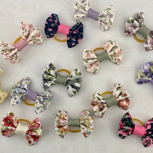 May include: A collection of 12 floral print hair scrunchies with different colored elastic bands. The scrunchies are made of fabric with a variety of floral patterns and colors, including pink, blue, green, yellow, and purple.