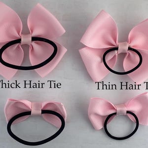 May include: Three pink hair bows with different sized elastic hair ties. The top left bow has a thick hair tie, the top right bow has a thin hair tie, and the bottom bow has a medium sized hair tie.  The text "Thick Hair Tie", "Thin Hair Tie" is visible below the bows.