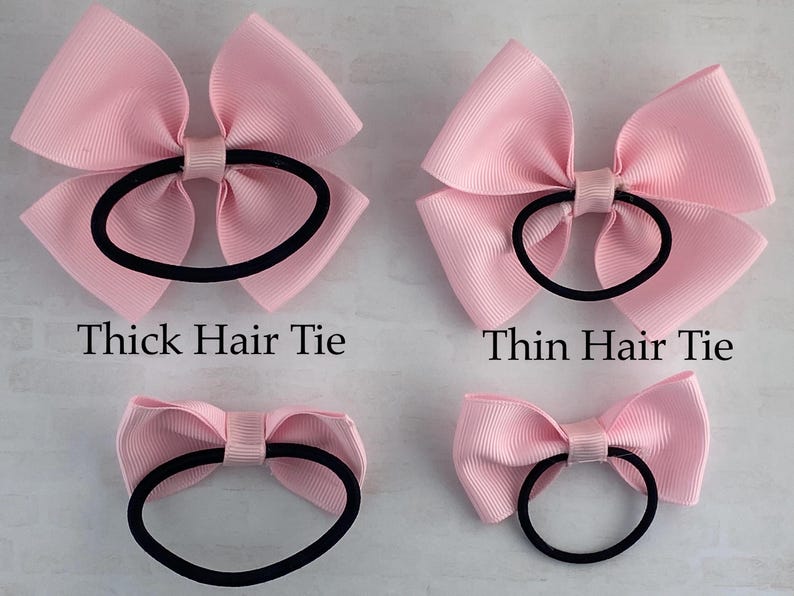 May include: Three pink hair bows with different sized elastic hair ties. The top left bow has a thick hair tie, the top right bow has a thin hair tie, and the bottom bow has a medium sized hair tie.  The text "Thick Hair Tie", "Thin Hair Tie" is visible below the bows.