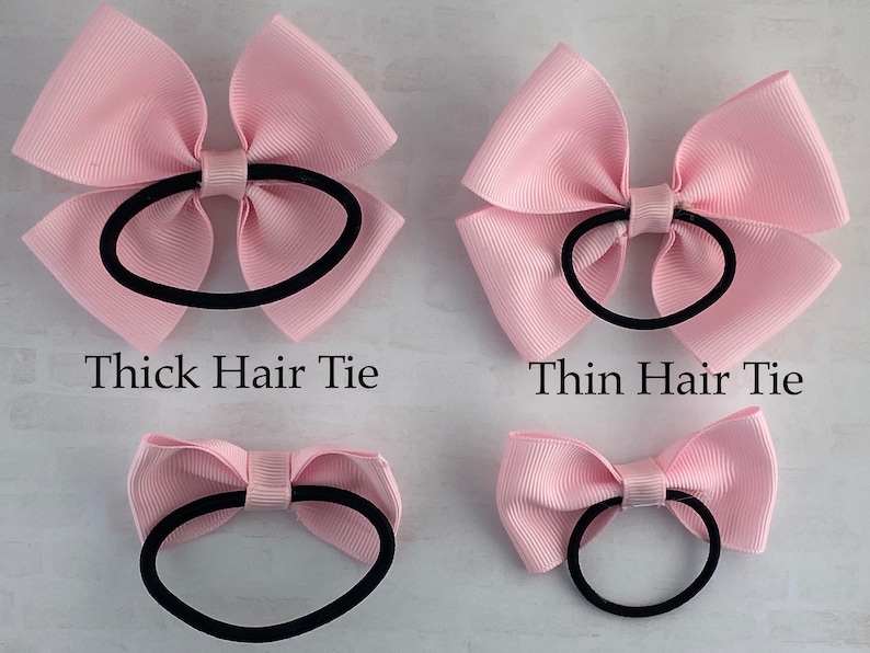 May include: Two pink hair bows with black hair ties. The top bow is larger and has a thicker hair tie. The bottom bow is smaller and has a thinner hair tie.  Thick Hair Tie and Thin Hair Tie are written below the bows.