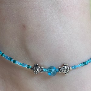 May include: A blue and green beaded anklet with two silver turtle charms and a blue glass bead.