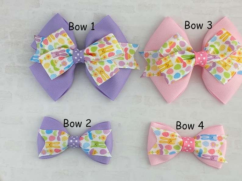 Pu&ograve; includere: Quattro fiocchi per capelli a tema pasquale di diverse dimensioni. I fiocchi sono realizzati in nastro viola e rosa con un motivo di uova di Pasqua e coniglietti bianchi e gialli. I fiocchi sono etichettati "Bow 1", "Bow 2", "Bow 3" e "Bow 4".