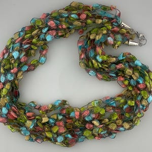 May include: A multi-colored crocheted necklace with a silver clasp. The necklace is made of a variety of shades of green, blue, and pink.