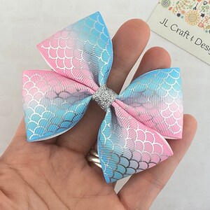 May include: A blue and pink ombre hair bow with a mermaid scale pattern and a silver glitter center.  JL Craft & Design.