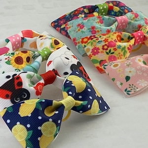 May include: Five colorful hair scrunchies with different floral and cartoon patterns. The scrunchies are made of fabric and have a rubber band.