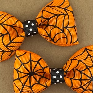 Puede incluir: Dos lazos para el pelo de color naranja y negro con estampado de telara&ntilde;a y centros de lunares negros y blancos.