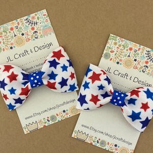 May include: Two red, white, and blue star-patterned hair bows with blue polka dot centers. The bows are displayed on white cards with the text "JL Craft & Design" and a website address.
