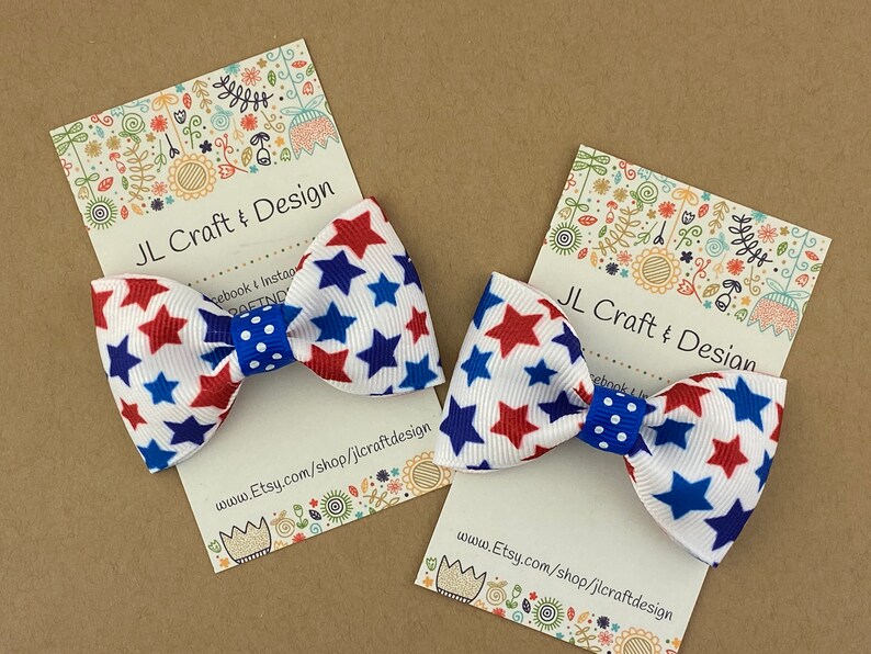 May include: Two red, white, and blue star-patterned hair bows with blue polka dot centers. The bows are displayed on white cards with the text "JL Craft & Design" and a website address.