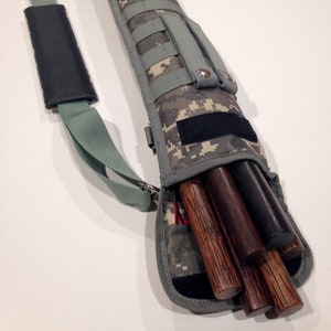 May include: A camouflage-patterned carrying case with a shoulder strap and multiple pockets. The case is open and contains several wooden staffs.