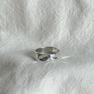 May include: A silver ring with a textured, uneven surface. The ring is wide and has a smooth, polished finish. The ring is set against a white, textured background.