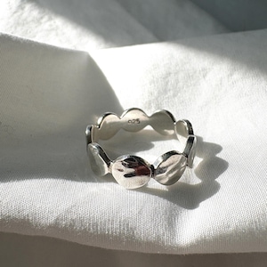 May include: A silver ring featuring a repeating pattern of oval shapes. The ring is made of a shiny metal and is set against a white background. The ring has the marking "925".