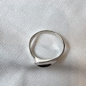May include: A silver ring with a smooth, curved design. The ring has a polished finish and a simple, elegant style. The ring is shown on a white, textured surface.