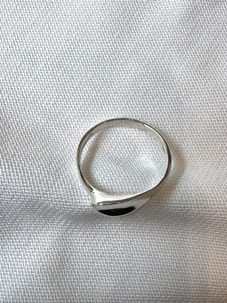May include: A silver ring with a smooth, curved design. The ring has a polished finish and a simple, elegant style. The ring is shown on a white, textured surface.