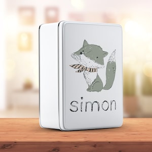 Op de afbeelding: Wit metalen blik met een groene vos die een gestreepte sjaal draagt en de naam "simon" op de voorkant.