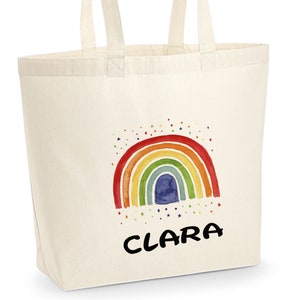 May include: A white canvas tote bag with a rainbow and stars design. The name "CLARA" is printed in black below the rainbow.