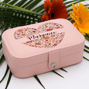 Peut inclure: Une boîte à bijoux rose avec un motif floral en forme de cœur sur le couvercle. Le mot "Margaux" est écrit au centre du cœur. La boîte rectangulaire a un fermoir argenté. Des fleurs et de la verdure sont en arrière-plan.