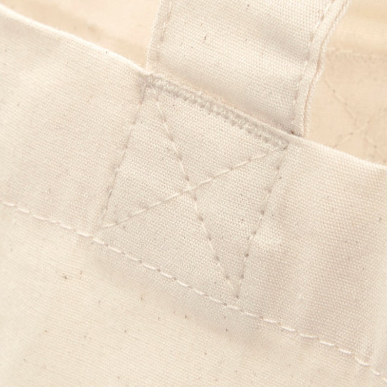 May include: Close-up of a white canvas tote bag with a reinforced stitched handle.