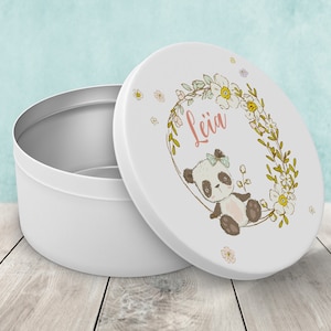 Peut inclure: Boîte de rangement en métal blanc avec un motif floral et un panda. Le couvercle porte le nom "Leïa" écrit en rose.