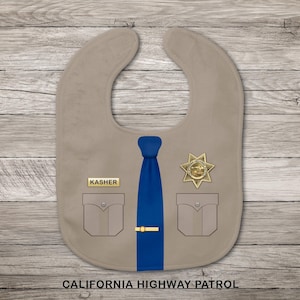 Könnte beinhalten: Ein beigefarbenes Baby-Lätzchen im Design einer Polizeiuniform mit einer blauen Krawatte, einer goldenen Krawattennadel, zwei Brusttaschen, einem goldenen sternförmigen Abzeichen und einem Namensschild mit der Aufschrift KASHER. CALIFORNIA HIGHWAY PATROL steht darunter.