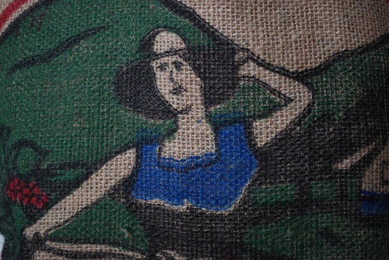 May include: A burlap fabric with a painted image of a woman wearing a blue top. The woman has dark hair and is looking to the right. The background is green and brown.