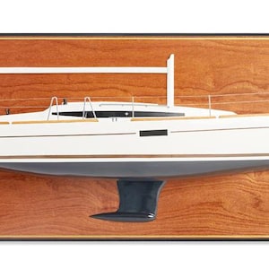 Könnte beinhalten: Ein Holzmodell eines weißen Segelboots mit blauem Rumpf, montiert auf einer Holzplatte. Die Platte hat einen goldenen Rand und der Text "Jeanneau Sun Odyssey 349" ist auf der Platte gedruckt.