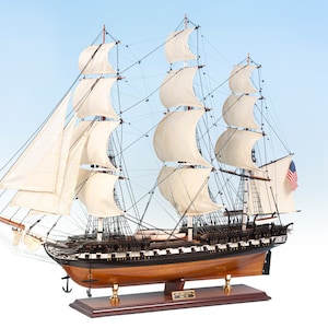 May include: A detailed wooden model of the USS Constitution, a historic American warship. The model features intricate details, including sails, rigging, and cannons. The ship is displayed on a wooden base with a nameplate.