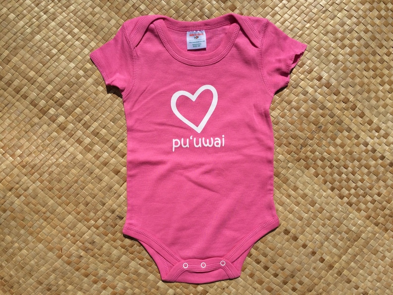 May include: Pink baby onesie with a white heart and the text "pu'uwai" on the front.