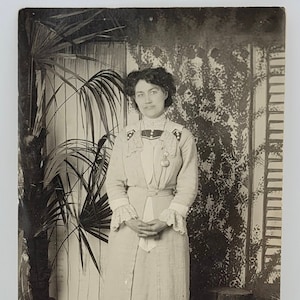 Datée 1914 CPRP, femme de l'époque édouardienne posant avec une grande plante et une toile de fond intéressante ~ Carte postale photo