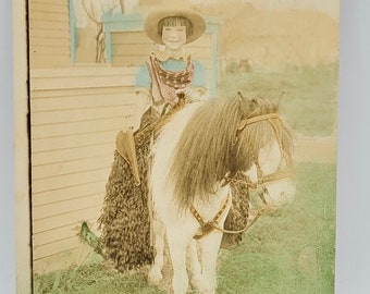 RPPC~Paula en un pony Shetland vistiendo chaparreras de lana y ropa occidental~Foto coloreada a mano