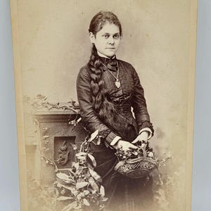 Mujer joven con trenza de pelo largo ~ Foto de gabinete ~ Sosteniendo una cesta ~ Lleva un colgante ~ Accesorios de follaje