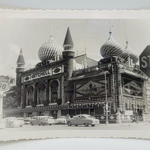 Könnte beinhalten: Ein Schwarzweißfoto eines Gebäudes mit einer verspielten, verzierten Fassade. Das Gebäude hat mehrere Türme und Kuppeln, und die Fassade ist mit komplizierten Details verziert. Ein Schild am Gebäude lautet "Mitchell". Ein Stoppschild ist im Vordergrund sichtbar.