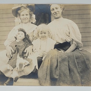Ragazza che tiene in mano una grande bambola ~RPPC~ Donna e due ragazze in posa all'aperto sui gradini del portico