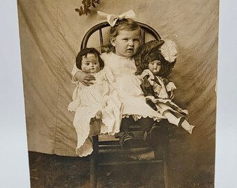 Kleines Mädchen mit Puppen ~ RPPC süsse Mädchen Haarschleife ~ Posed Outdoors Behelfskulisse ~ Foto Postkarte